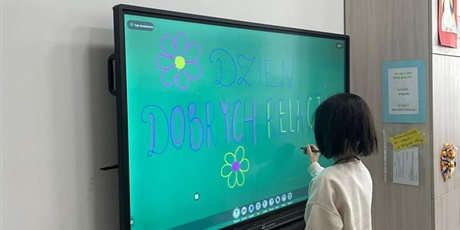Powiększ grafikę: dziewczynka pisze na tablicy multimedialnej - napis Dzień Dobrych Relacji